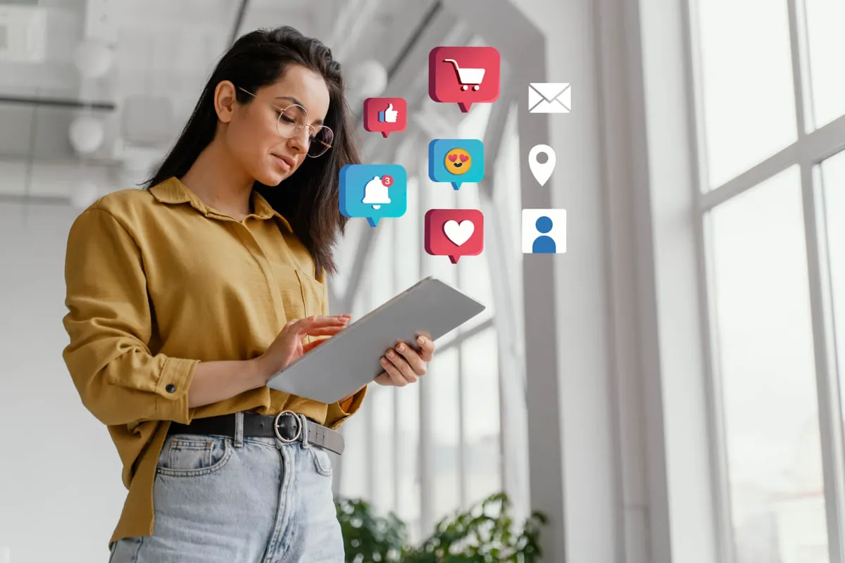 Woman wearing glasses uses a tablet surrounded by like, shopping cart and notification icons, symbolizing digital marketing