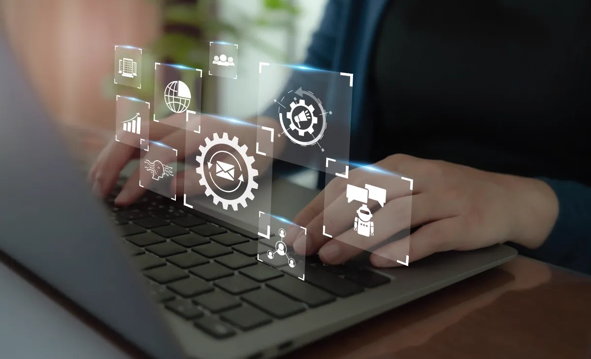 Hands typing on a laptop with floating marketing automation icons of gears, email, a chart, and a chatbot
