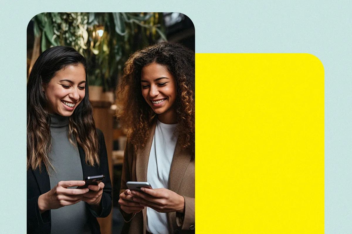 Two smiling women look at their phones side by side, as if exchanging a digital business card
