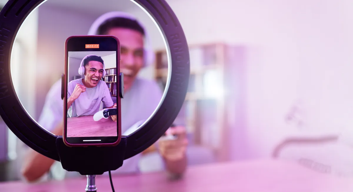 Phone on a ring light filming a young person with headphones celebrating with a video game controller, an influencer marketing scene