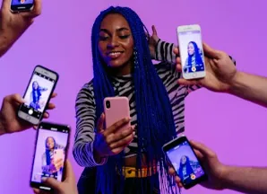 Young woman with blue braids holding a phone, surrounded by hands with smartphones taking her picture, representing a strong online presence
