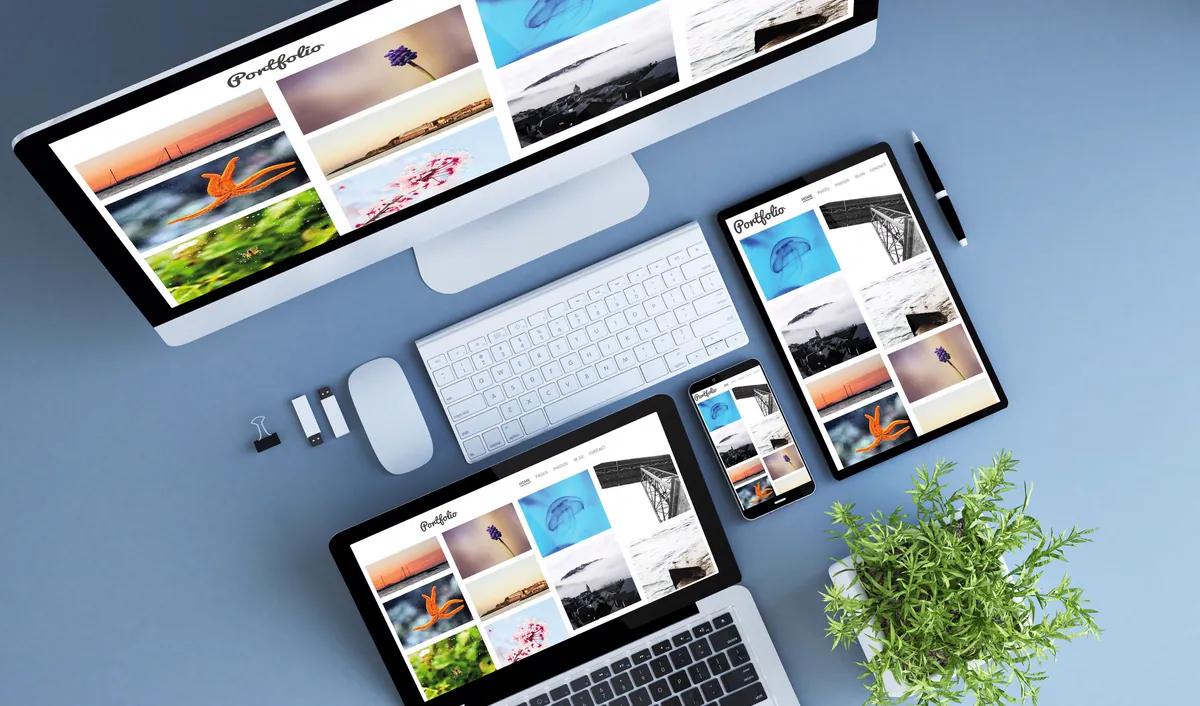 Desktop computer, laptop, tablet and smartphone on a blue table displaying the same minisite as a photo gallery, like a digital catalog