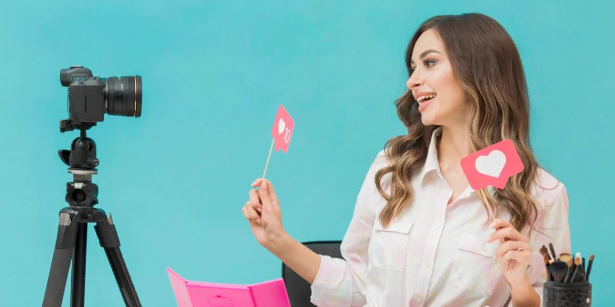 Smiling woman holding like signs in front of a camera on a tripod, as a content creator pitching herself to brands