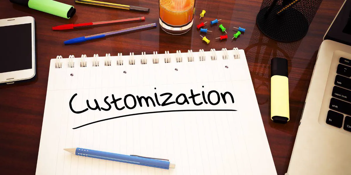 Notebook with the word Customization handwritten on it, on a desk with a laptop, phone and pens, illustrating the idea of customizing your minisite