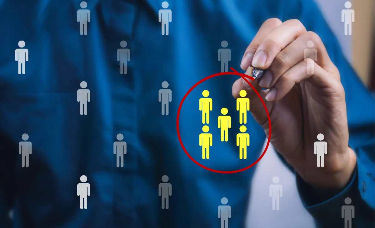 Hand holding a pen circles in red five yellow people icons among gray icons, illustrating niche marketing