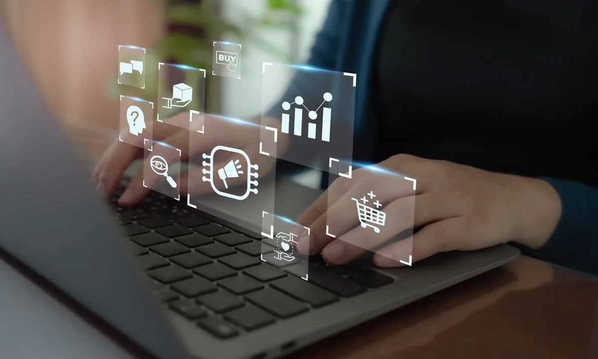 Hands typing on a laptop with virtual marketing, chart, and shopping cart icons, suggesting automation and digital productivity