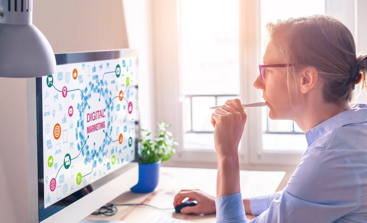 Thoughtful woman with glasses in front of a monitor showing a digital marketing diagram, planning online advertising