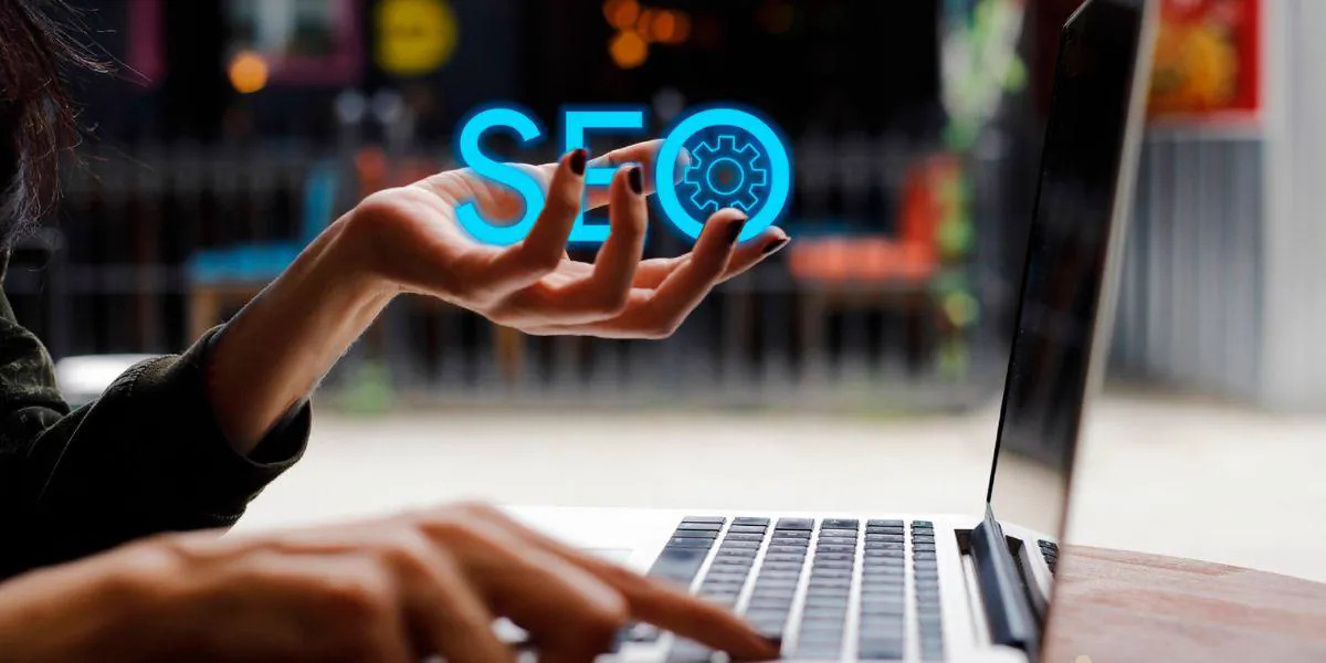 Woman typing on a laptop while her other hand displays the word SEO in blue neon with a gear icon