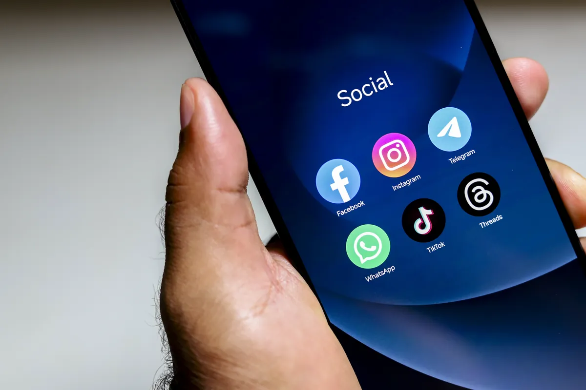 Hand holding a phone with a Social folder and social media apps like Instagram, TikTok, WhatsApp and Facebook