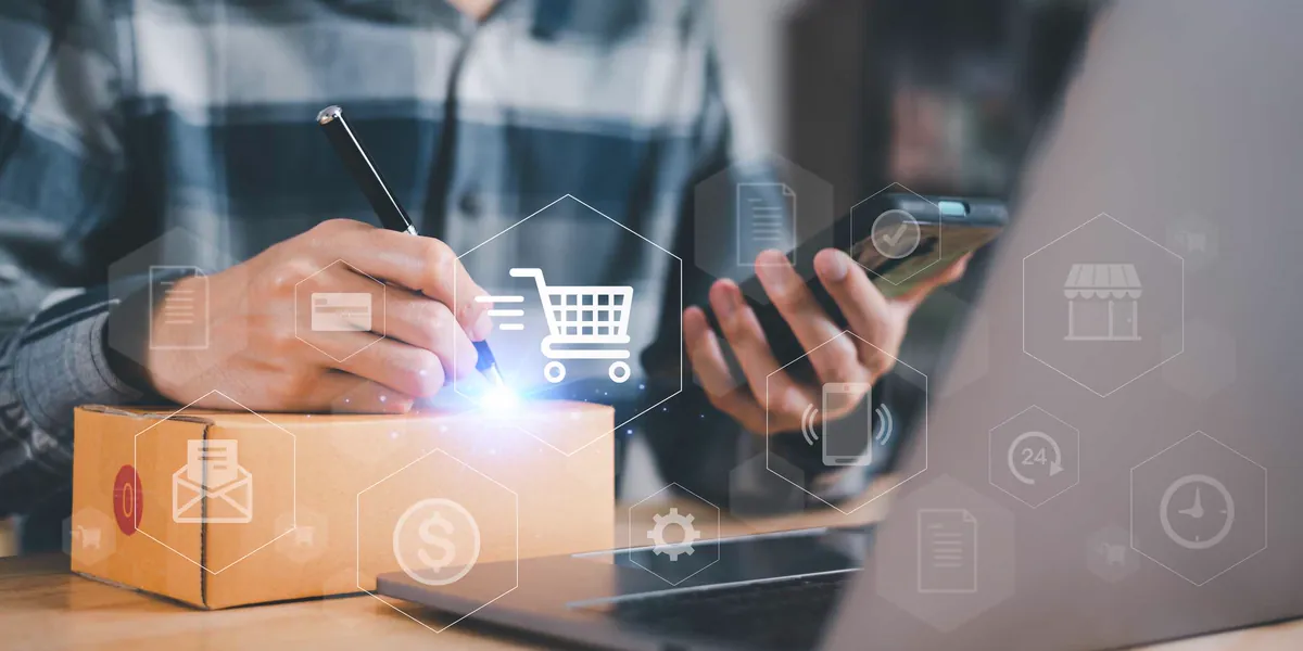 Person writing on a cardboard box while holding a phone, with shopping cart and payment icons over an online sales channel