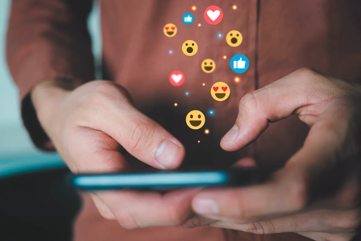 Hands using a smartphone with like, heart, and emoji icons floating around, suggesting brand engagement on social media