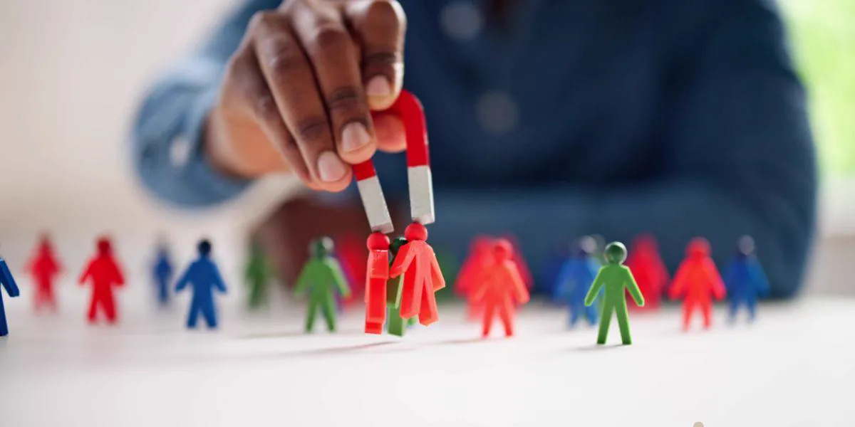 Hand holding a magnet that attracts red figures among colorful figures, symbolizing lead attraction and conversion