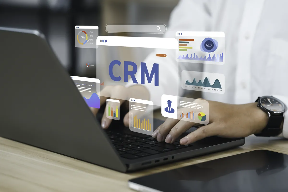 Hands typing on a laptop with virtual CRM screens and charts, automation tools for business