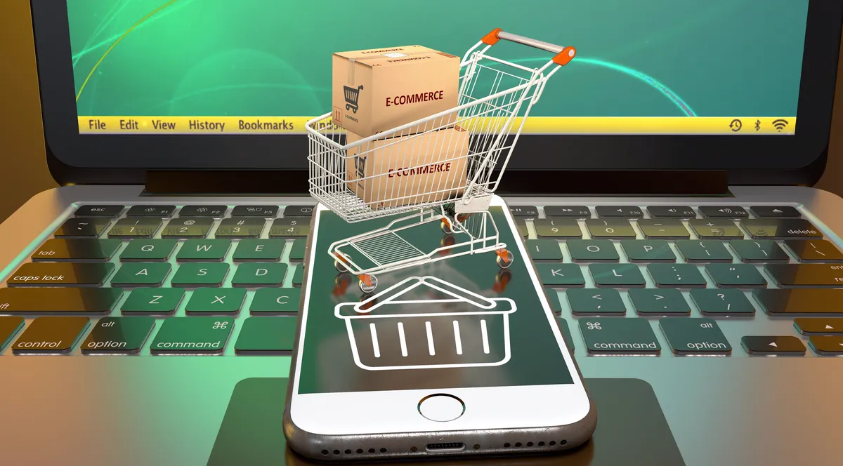 Miniature shopping cart with e-commerce boxes on a smartphone resting on a laptop keyboard